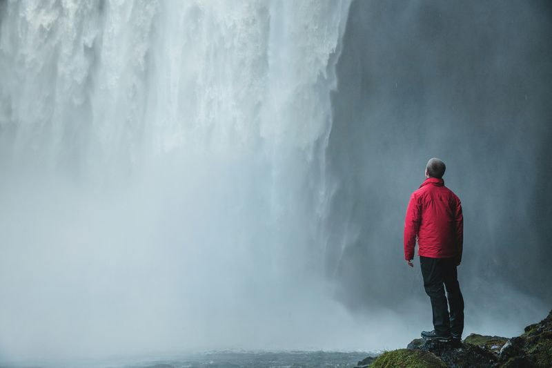 A person standing alone in front of a massive waterfall.