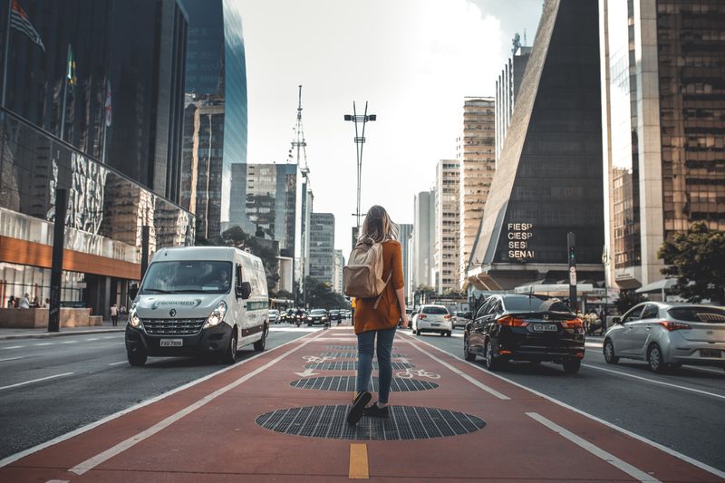 Girl is standing alone in the middle of the road surrounded by cars and buildings