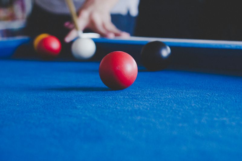 A red billiard ball on a pool table as a player aims a cue stick to take a shot.