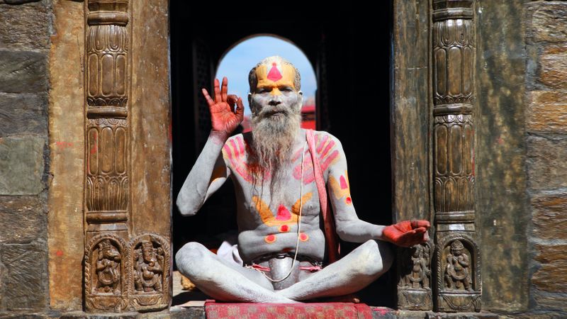 'Indian man sitting in temple door way with right hand index and thumb touching in gyan mudra.'