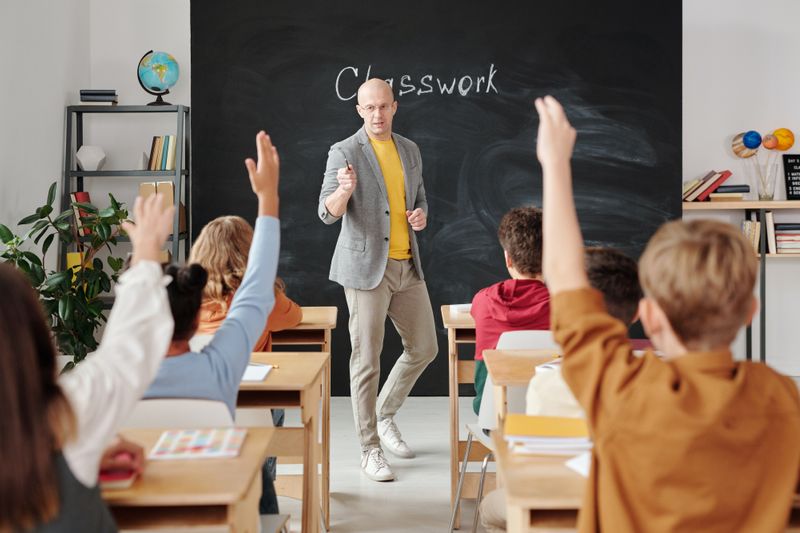 Photo of teacher teaching a class full of students raising their hands to participate