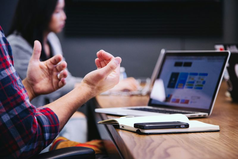 A person gesturing with their hands while looking at a laptop.