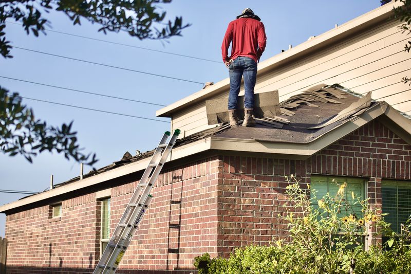 Person standing on residential roof looking at shingle damage.