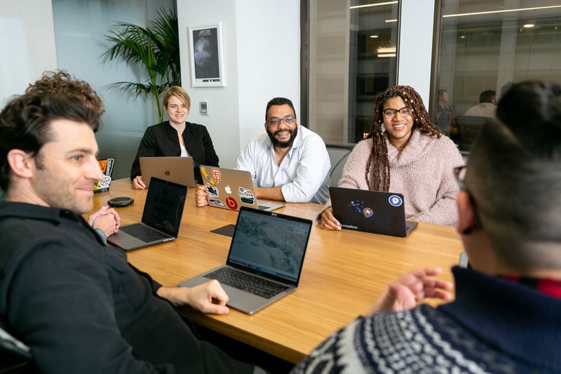 Diverse team of 5 people working on their laptops and collaborating with each other in an office