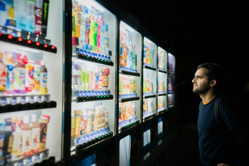 A man stares at a vending machine with many drink options. 