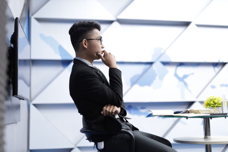 Man in an office scratching his chin, looking into the distance.