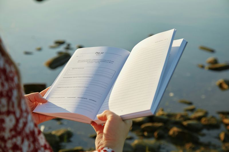 A woman holding a journal in front of a landscape.