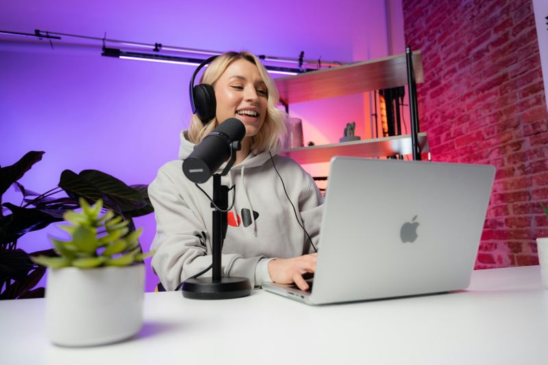 A woman happily recording a podcast on her laptop as a study technique.
