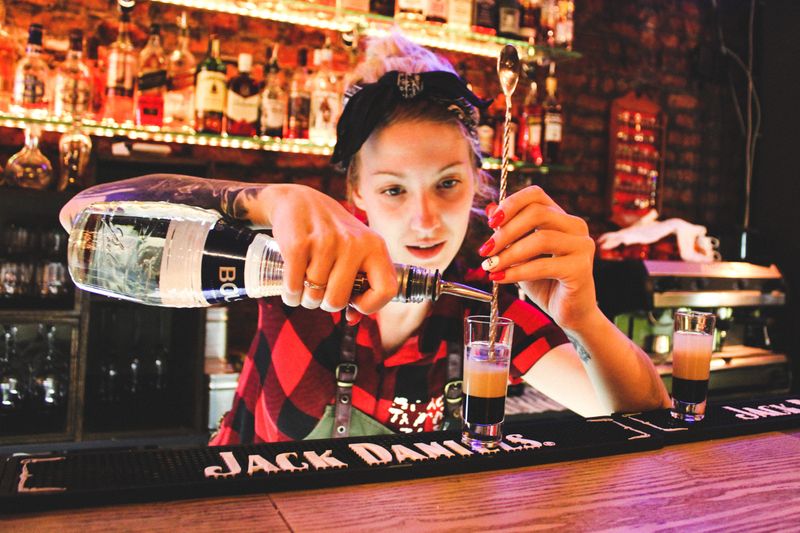 Woman bargender pouring ilquir into a thin glass that has layers of liquid.