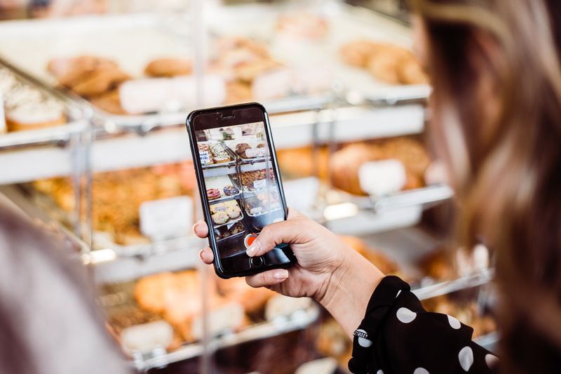 Up close image of an iPhone held by a woman taking a video of a bakery