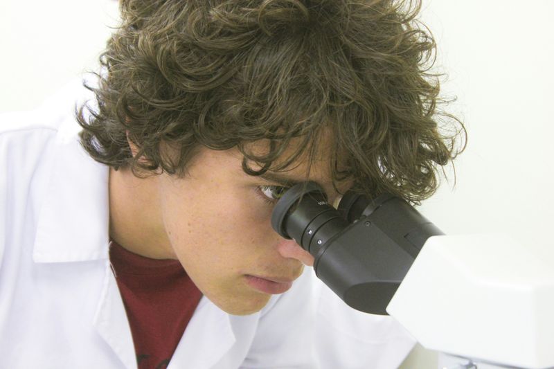 A biology student looks through a microscope in a lab.