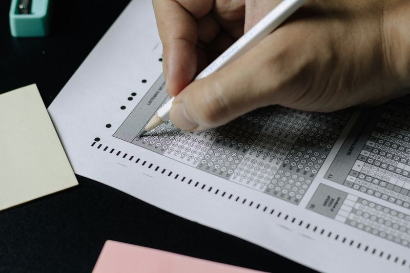 A person with a pencil filling in a response a response bubble on a scantron sheet.