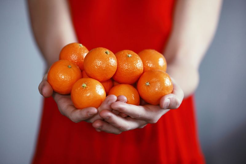 person in a red dress holding mandarin oranges in both of their hands. 