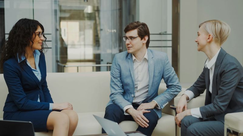 Three people seated on couches in an office, happily discussing work.