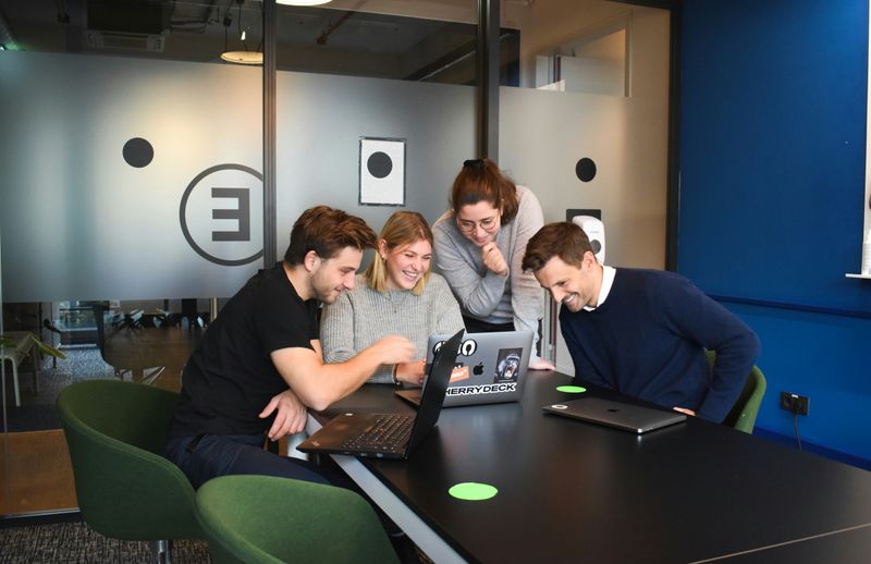 Four young people in an office space gathered around a laptop. 