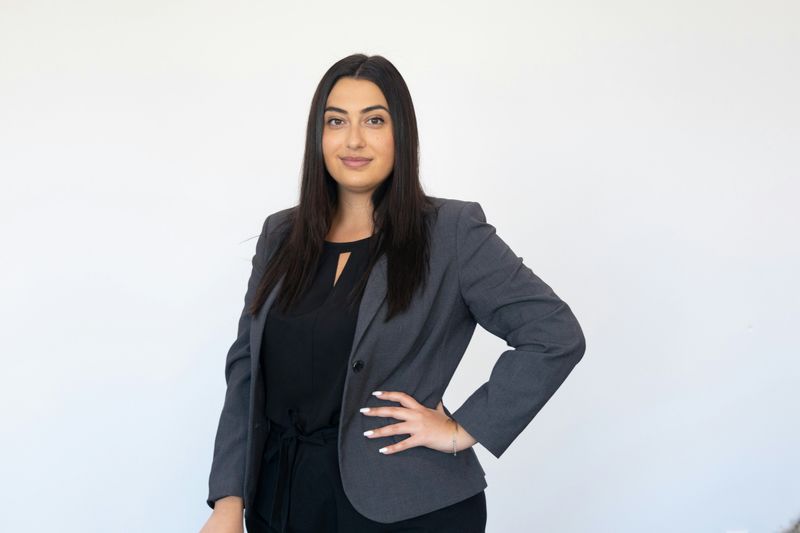 A women in a business suit, smiling, with one hand on her hip.