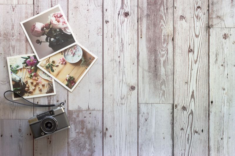 A rustic gray wooden surface with an old camera and 3 photos on it.
