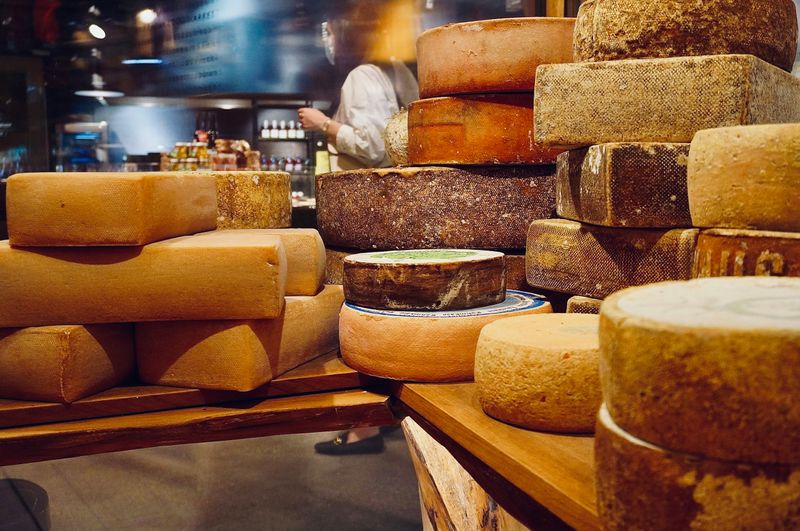 Many wheels of different types of cheese in a pile on a table.