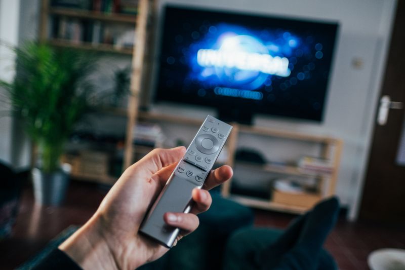 Image of hand holding a TV remote. The universal logo appears on a TV in the background
