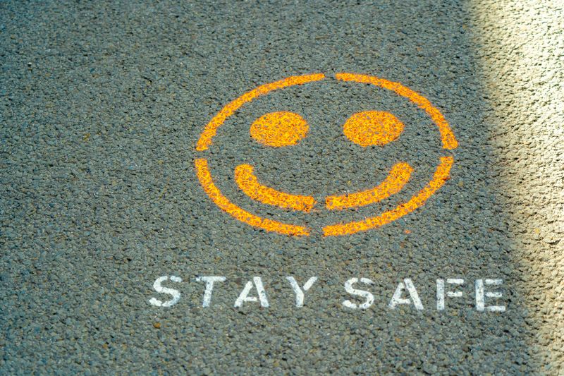 A painted smiley face on a road with the words “stay safe” stencilled under it.