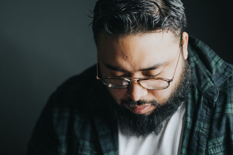 Man of colour with beard and glasses looking down pensive