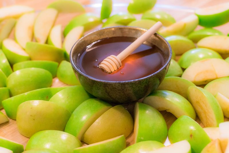 Sliced green apples with a bowl of honey in the middle.