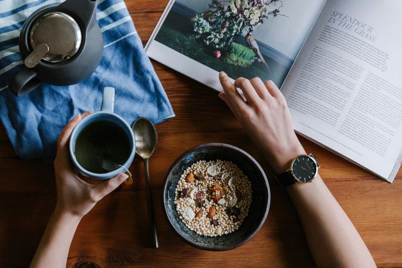 Person sitting at breakfast table have tea and cereal, reading a magazine.