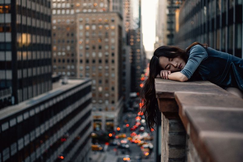 Asian female putting her face on her arms, closed eyes, on a balcony edge overlooking a city view