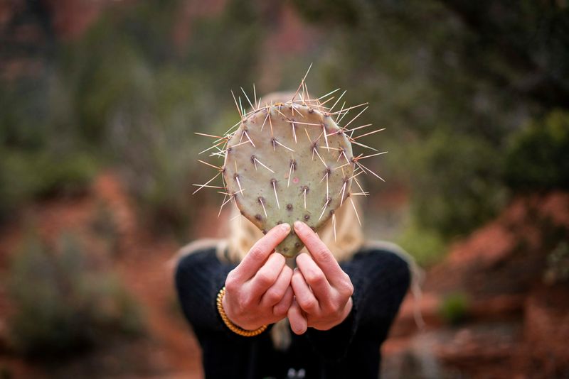 A woman holds a prickly cactus pad in front of her, hiding her face. 