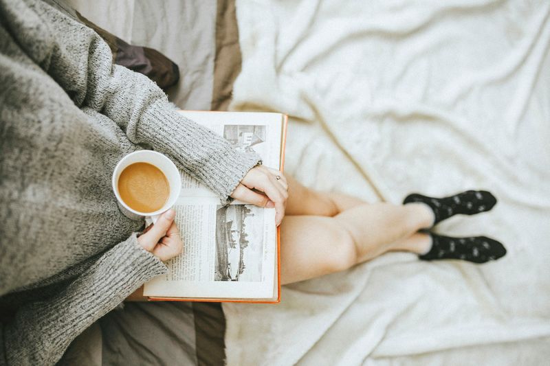 Person reading a book with a cup of coffee in hand.