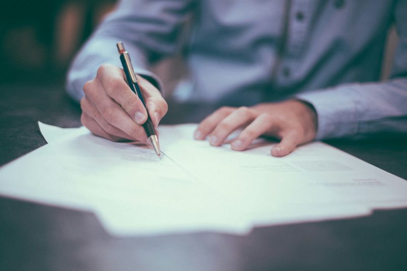 A person writing on three pieces of papers with a pen. 