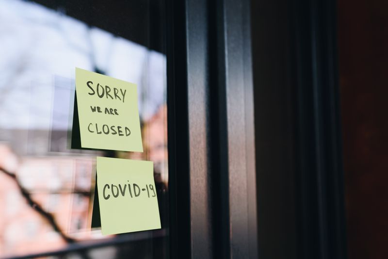 Two yellow post-its on a business door that read 'Sorry, we are closed' and 'Covid-19.'