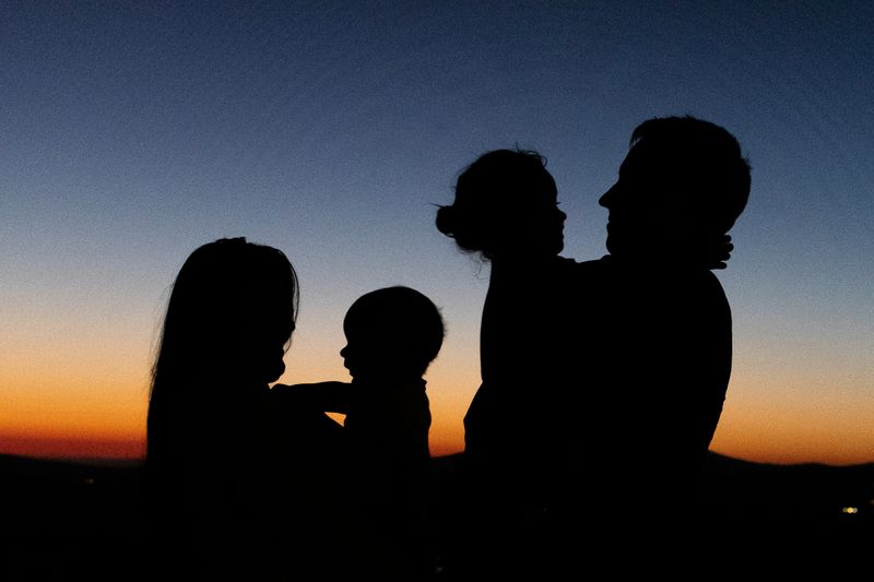 Silhouettes of a family of four people, outside at dusk or dawn.