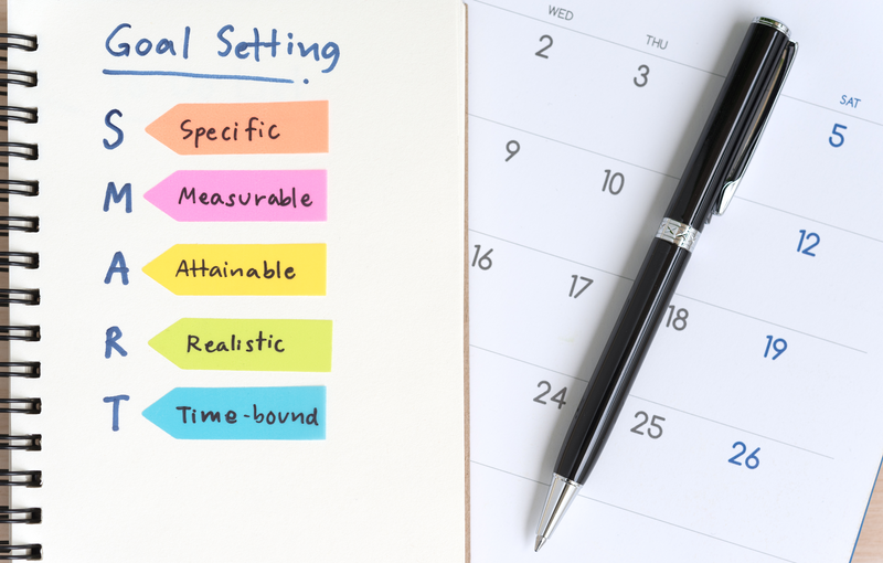 A calendar with a pen next to notes on SMART Goal Setting: Specific, Measurable, Attainable, Realistic, Time-bound.