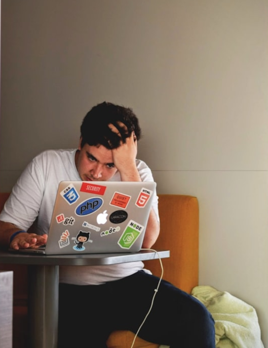 A guy looks stressed on his laptop, while grabbing his head with one of his hands