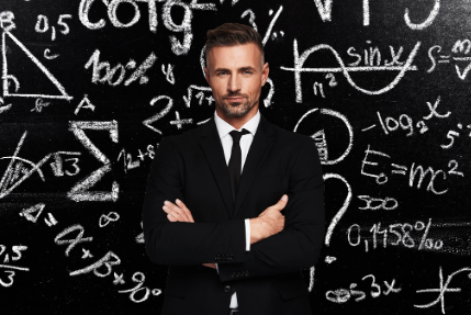 Image of a man in a formal black suit standing with his arms crossed in front of a black board.