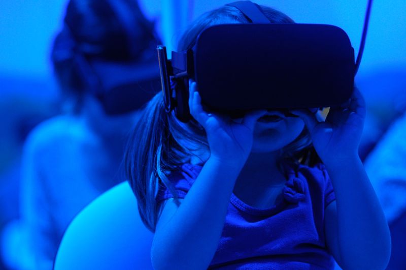 A young child wearing virtual reality goggles, gripping them firmly in both hands.