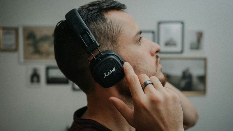 A man who is wearing an over-ear headphone is looking off to the distance.