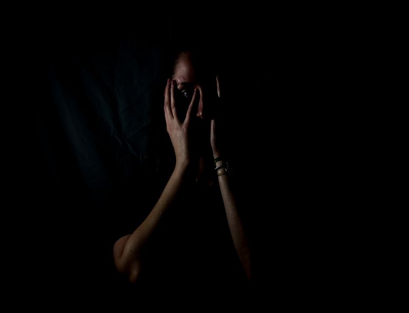 A person holding their hands to their face in a dark room.