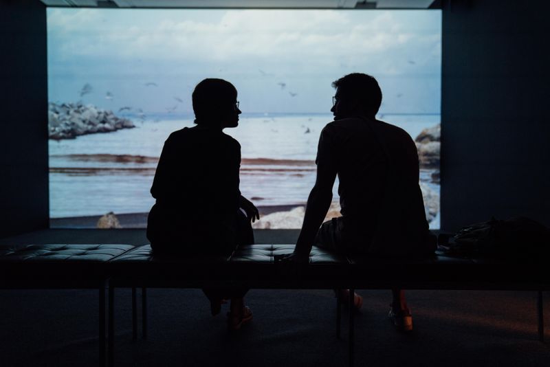 a couple is sitting in shadow talking in front of a large screen