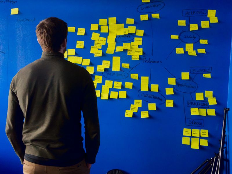 A person brainstorming solutions to a problem, looking at yellow sticky notes on a blue wall.