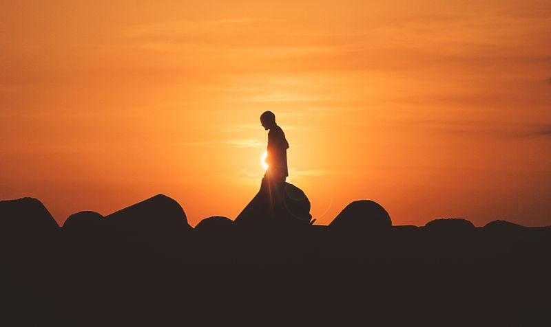 A silhoutte of a person standing on rocks at sunset.