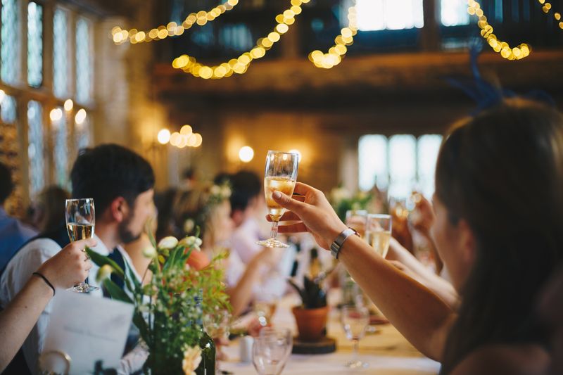 An out of focus picture of wedding guests with raised glasses for a toast at a wedding reception.