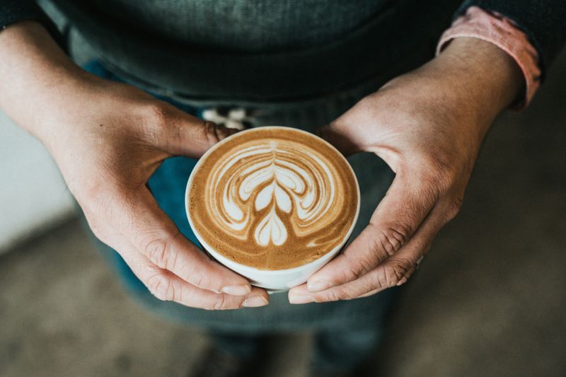 A person hold a cup of latte with hearts on it. 