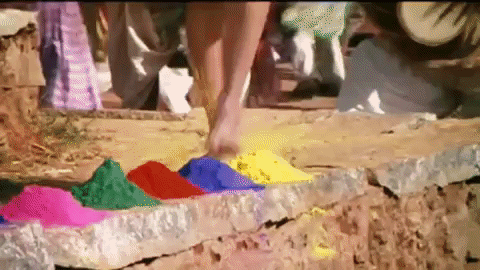 A woman running through piles of different colored powders and dyes, kicking them around
