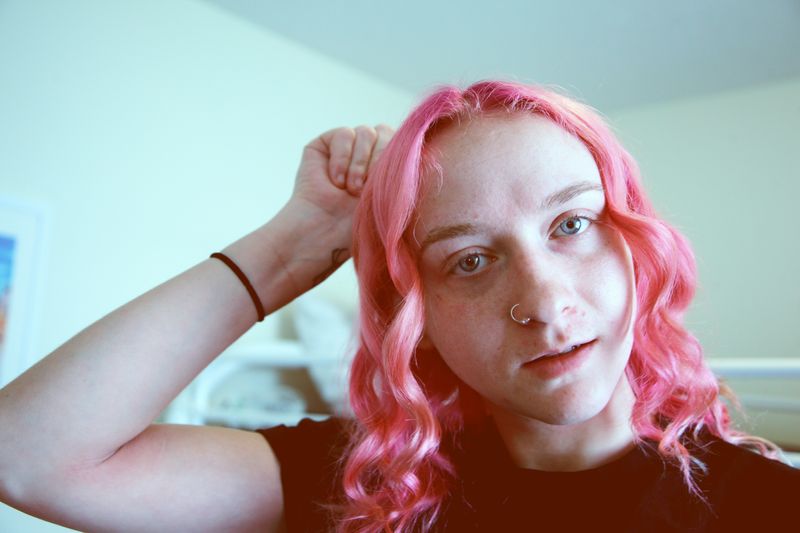 A person with pink hair and a nose piercing.