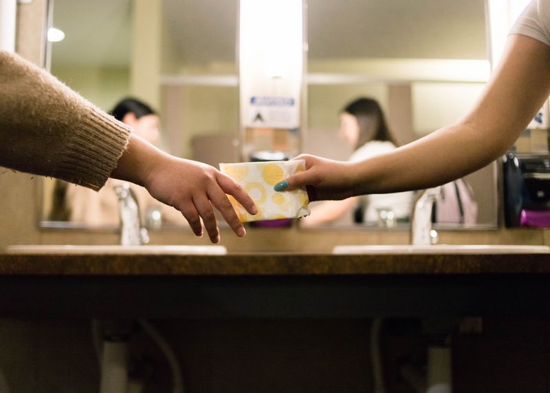 A woman handing another woman a menstrual pad package.