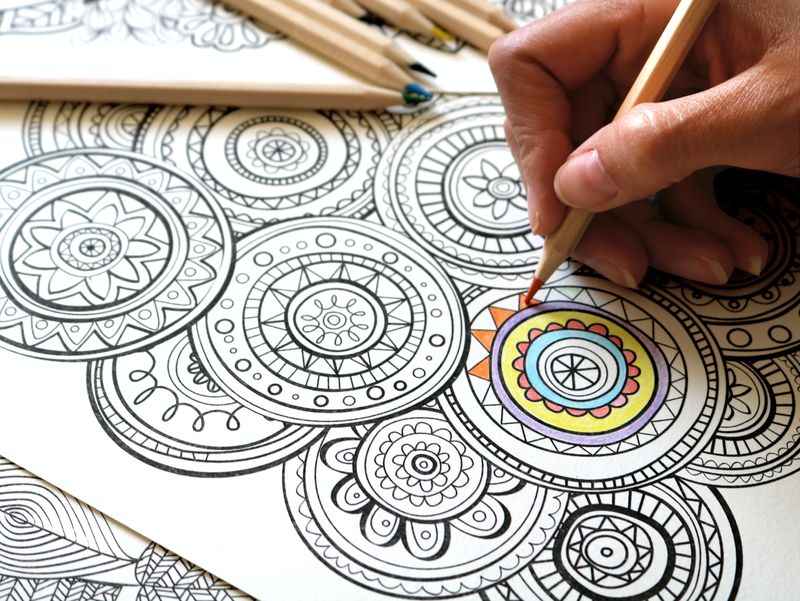A person, filling in patterns of a Mandala with an orange pencil crayon