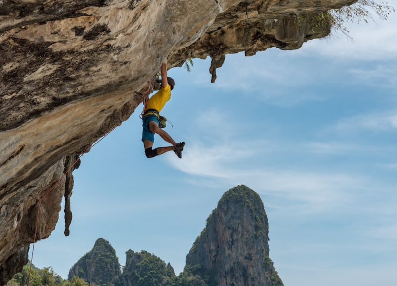 A person rock climbing,, handing precariously by just their hands. 