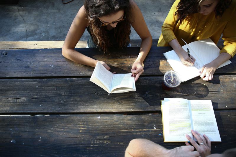 A group of students writing in notebooks on a picnic table.